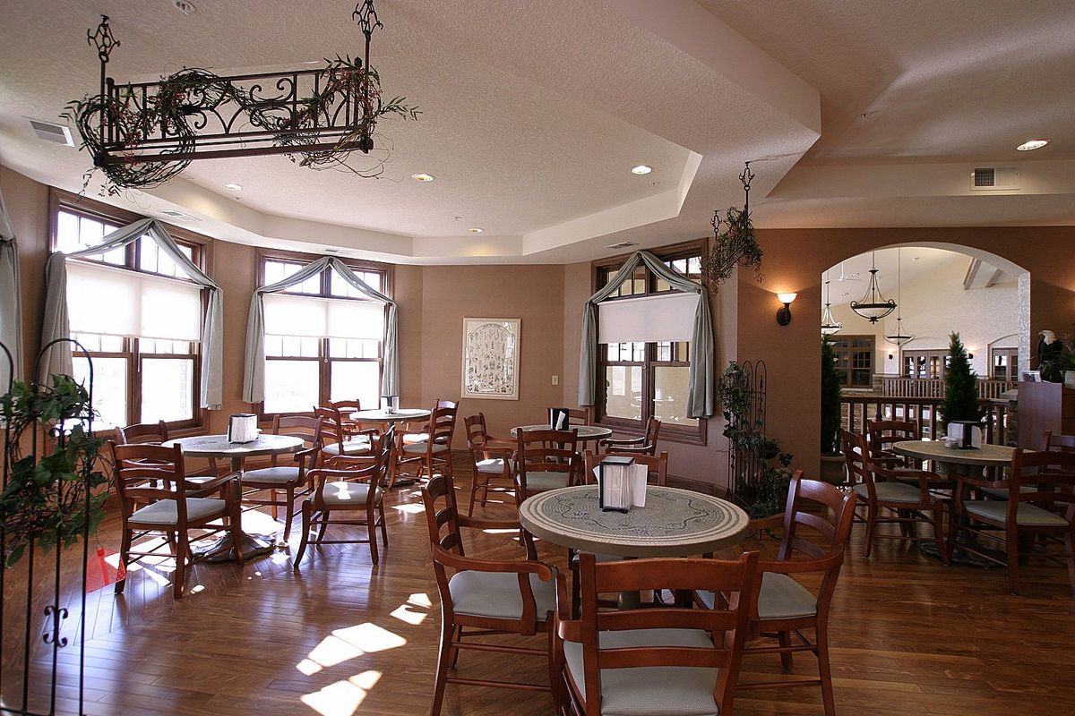 A cozy restaurant interior featuring multiple tables and chairs, with natural light streaming through large windows.