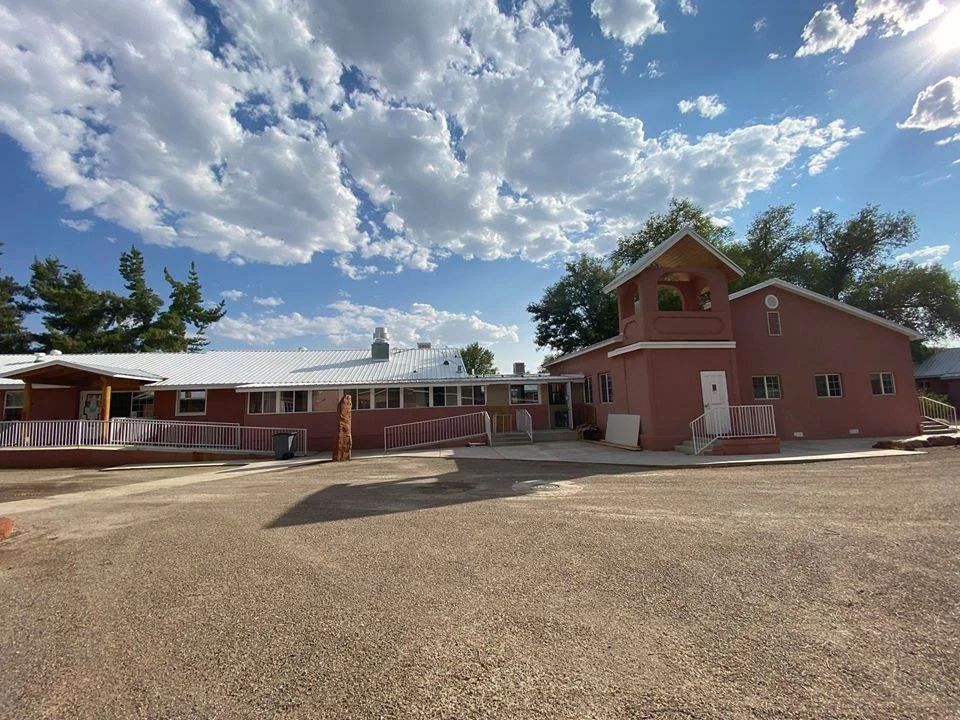 A brick building under a partly cloudy sky with trees in the background.