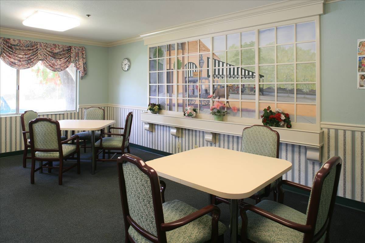 A cozy dining area with tables and chairs, featuring a wall mural and decorative plants.