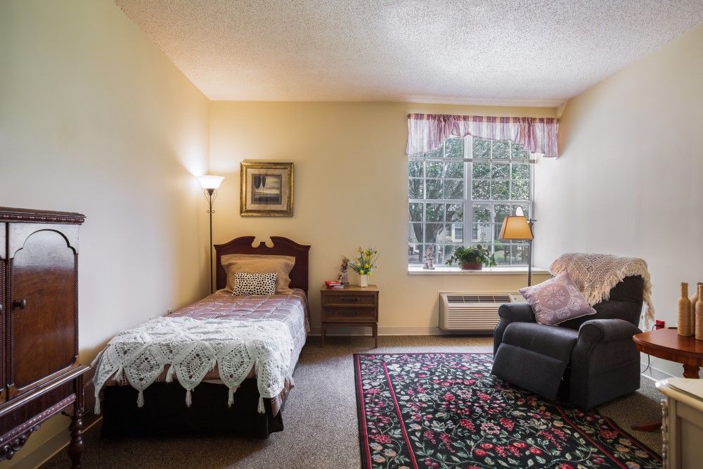 A cozy bedroom with a single bed, armchair, and a large window with pink curtains.