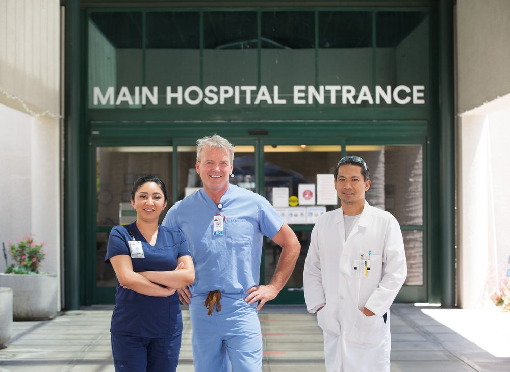 Medical professionals stand in front of the main hospital entrance.