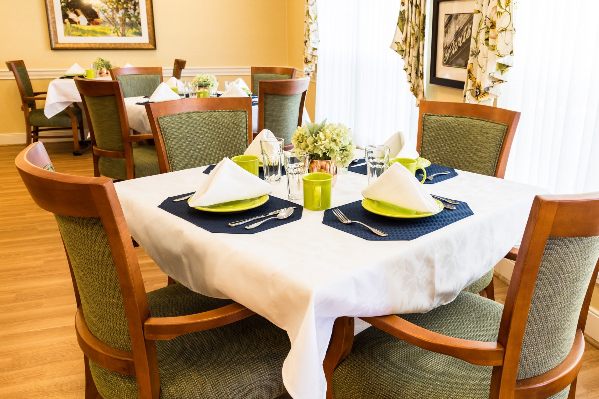 A neatly set dining table with green accents, complete with a floral centerpiece and cushioned chairs.