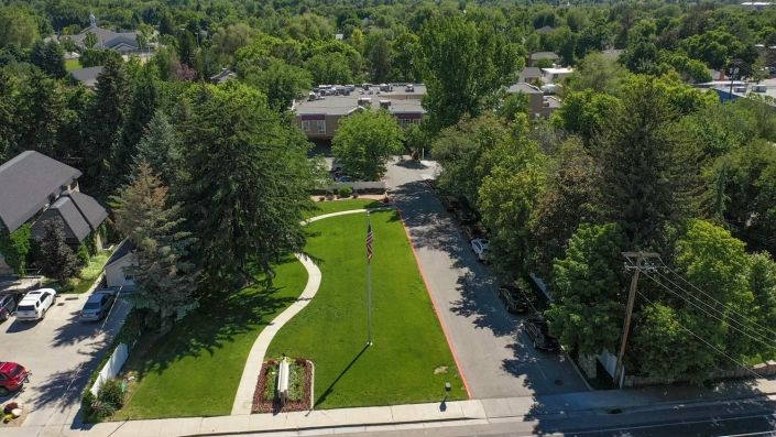 Aerial view of a park featuring a green lawn, winding pathways, and surrounding trees.