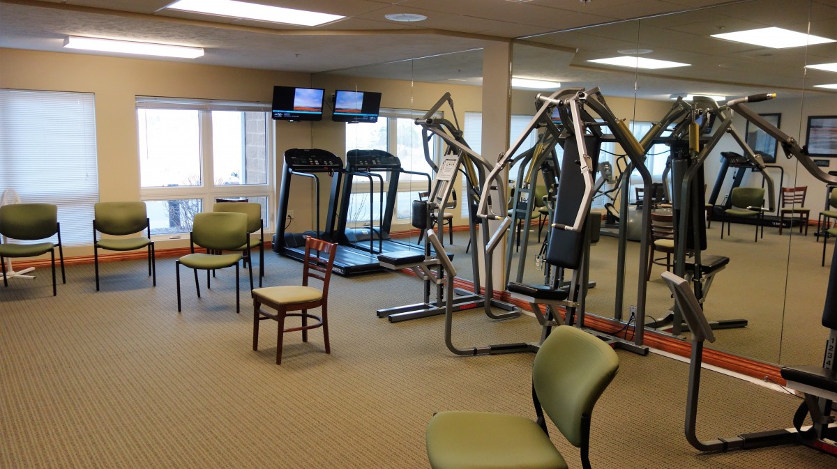 A gym with exercise equipment including treadmills and chairs, mirrored walls, and a spacious interior.