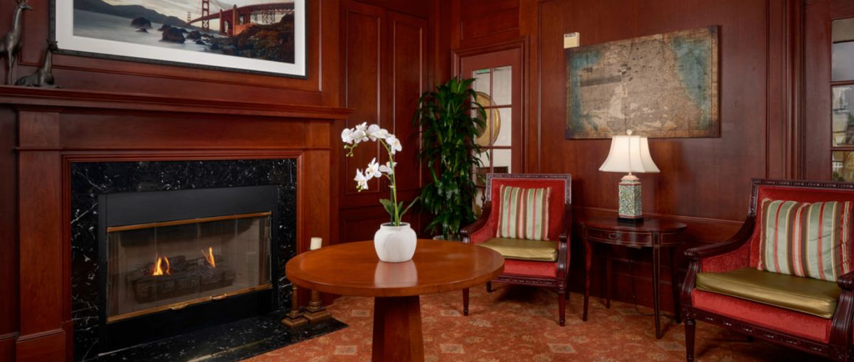 A cozy living room with wood paneling, featuring a fireplace and elegant decor including an orchid on a round table.