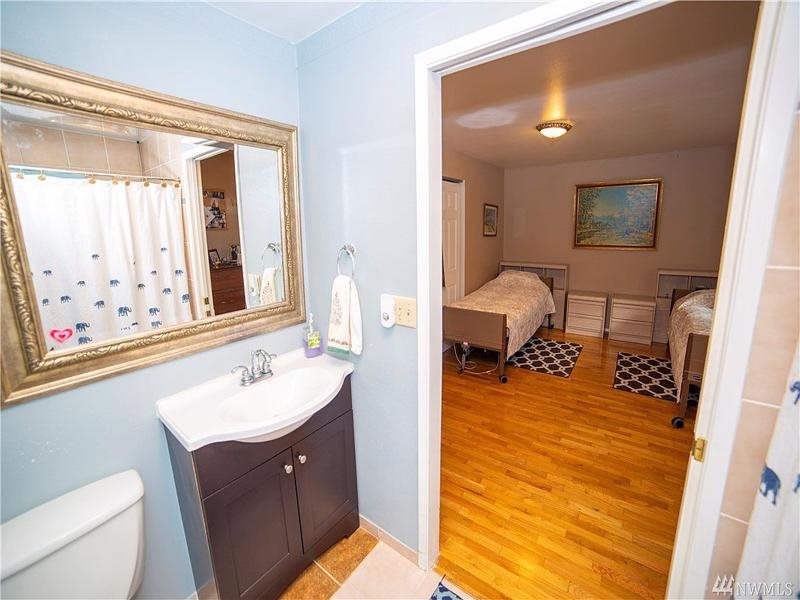 A view from a bathroom into a bedroom with two beds and hardwood flooring.