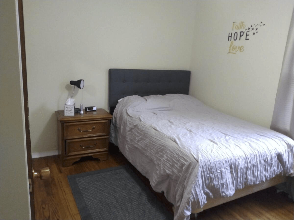 A cozy bedroom with a neatly made bed and a nightstand featuring a lamp and decor.