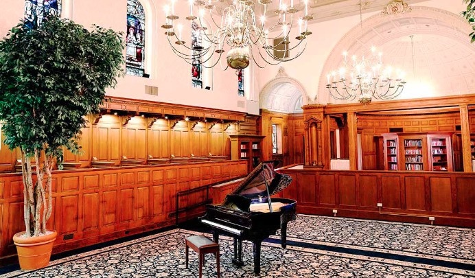 A grand piano in an elegant room with wooden paneling and stained glass windows.