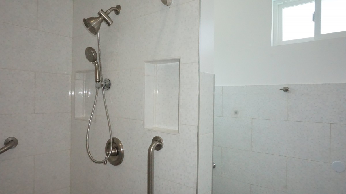 A modern bathroom shower with a showerhead, grab bar, and built-in shelf.