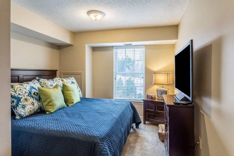 A cozy bedroom with a bed, desk, and TV near the window.