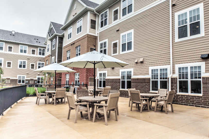 A well-furnished outdoor patio area with tables, chairs, and umbrellas in front of an apartment building.