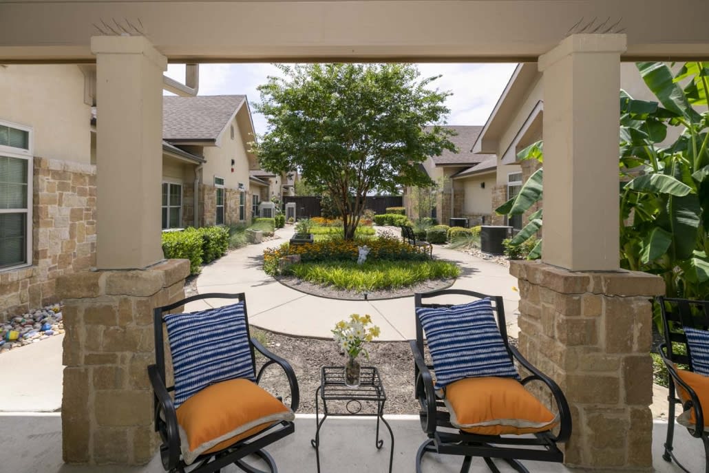 A peaceful courtyard with two chairs offering a view of the garden and tree.
