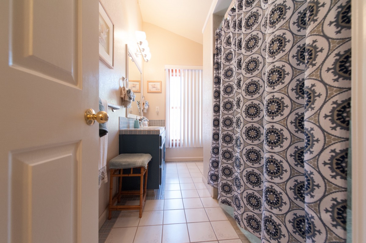 A well-lit bathroom featuring a patterned shower curtain, vanity with mirror, and tiled flooring.