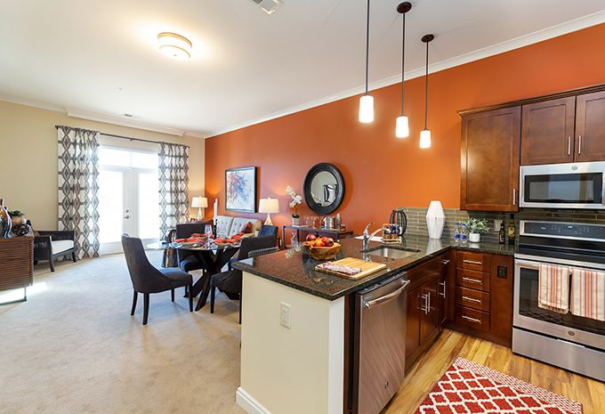 A modern open-concept kitchen and dining area with vibrant orange walls and stylish pendant lighting.
