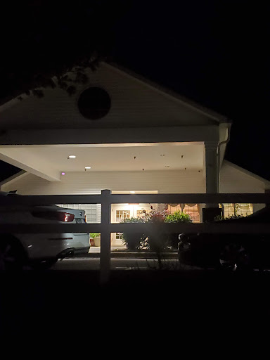 A well-lit house during the night, showcasing vehicles parked outside.