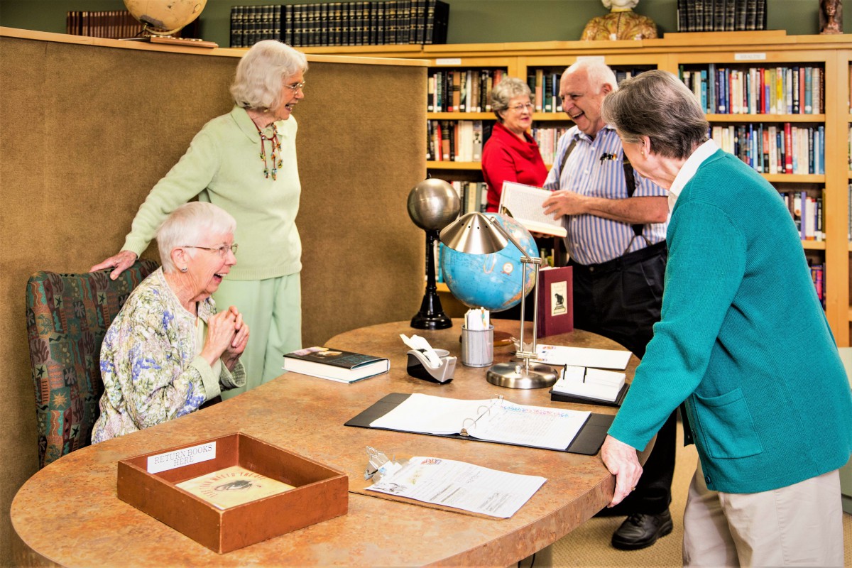 A group of seniors engage in a lively discussion around a table in a library setting.