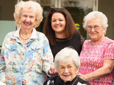 A group of women, including elderly individuals, smiling outside together.