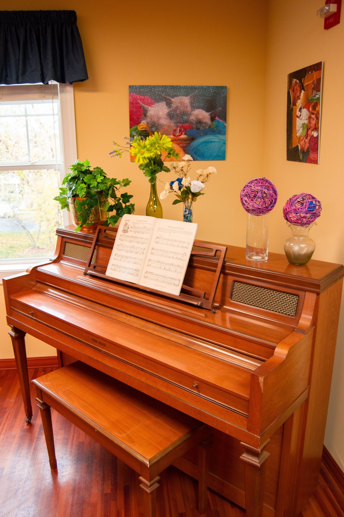 A cozy living room with a wooden piano adorned with sheet music and surrounded by decorative flowers.