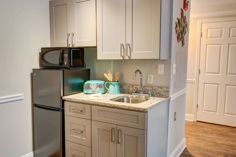 A compact kitchen area featuring a microwave, refrigerator, toaster, and sink with beige cabinets and a granite countertop.
