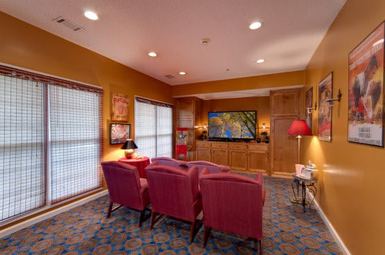 A cozy home theater setup with comfortable chairs facing a large TV, complemented by warm wood paneling and vibrant decor.