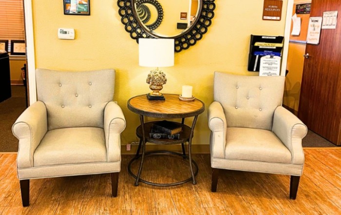 A cozy living room setup featuring two beige armchairs, a round table with a lamp, and a decorative mirror on the wall.