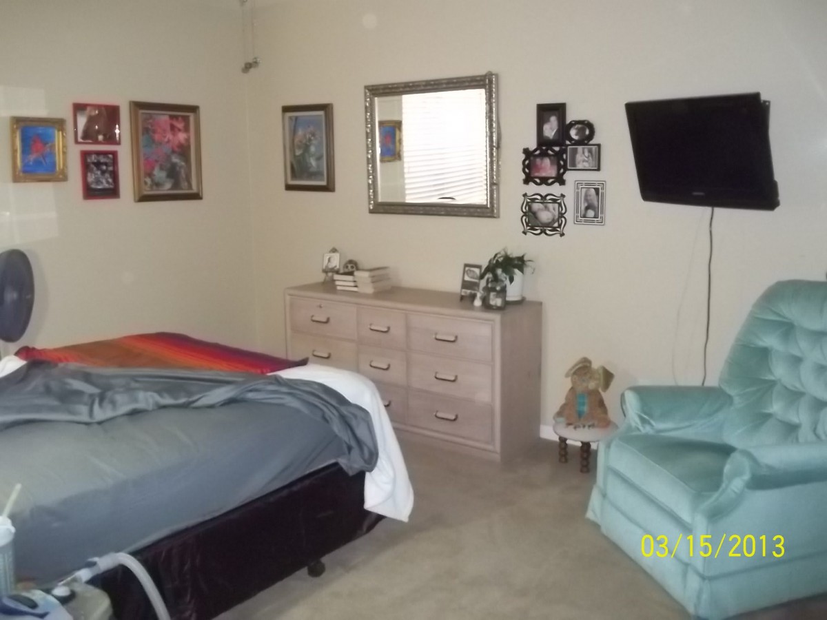 A cozy bedroom with a bed, dresser, mirror, and wall-mounted TV.