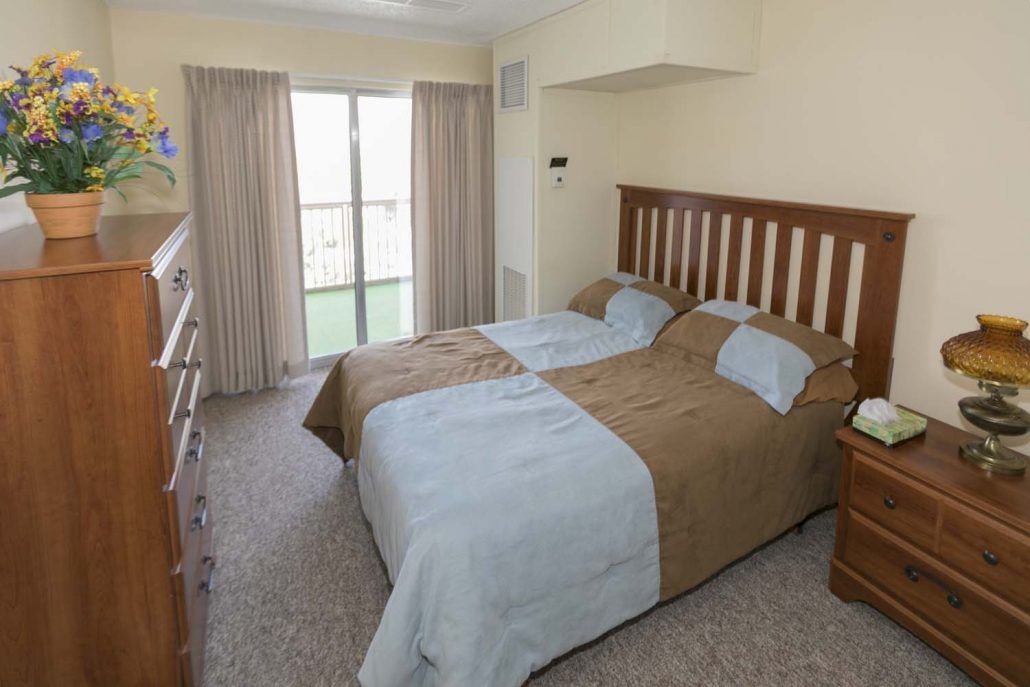 A cozy bedroom featuring a double bed with light blue and brown bedding, complemented by curtains over a large window.
