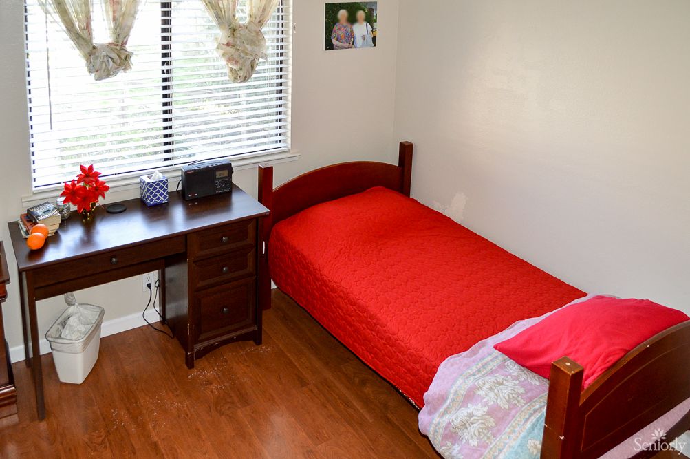 A tidy bedroom with a red bedspread and a wooden desk by the window.