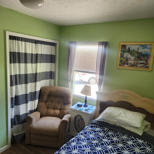A cozy bedroom featuring a comfortable armchair and a neatly made bed, accented by fresh green walls.