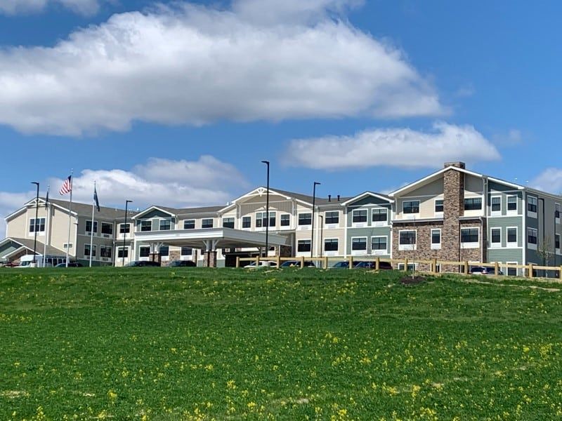A modern building set against a backdrop of blue sky and clouds, with a grassy field in the foreground.