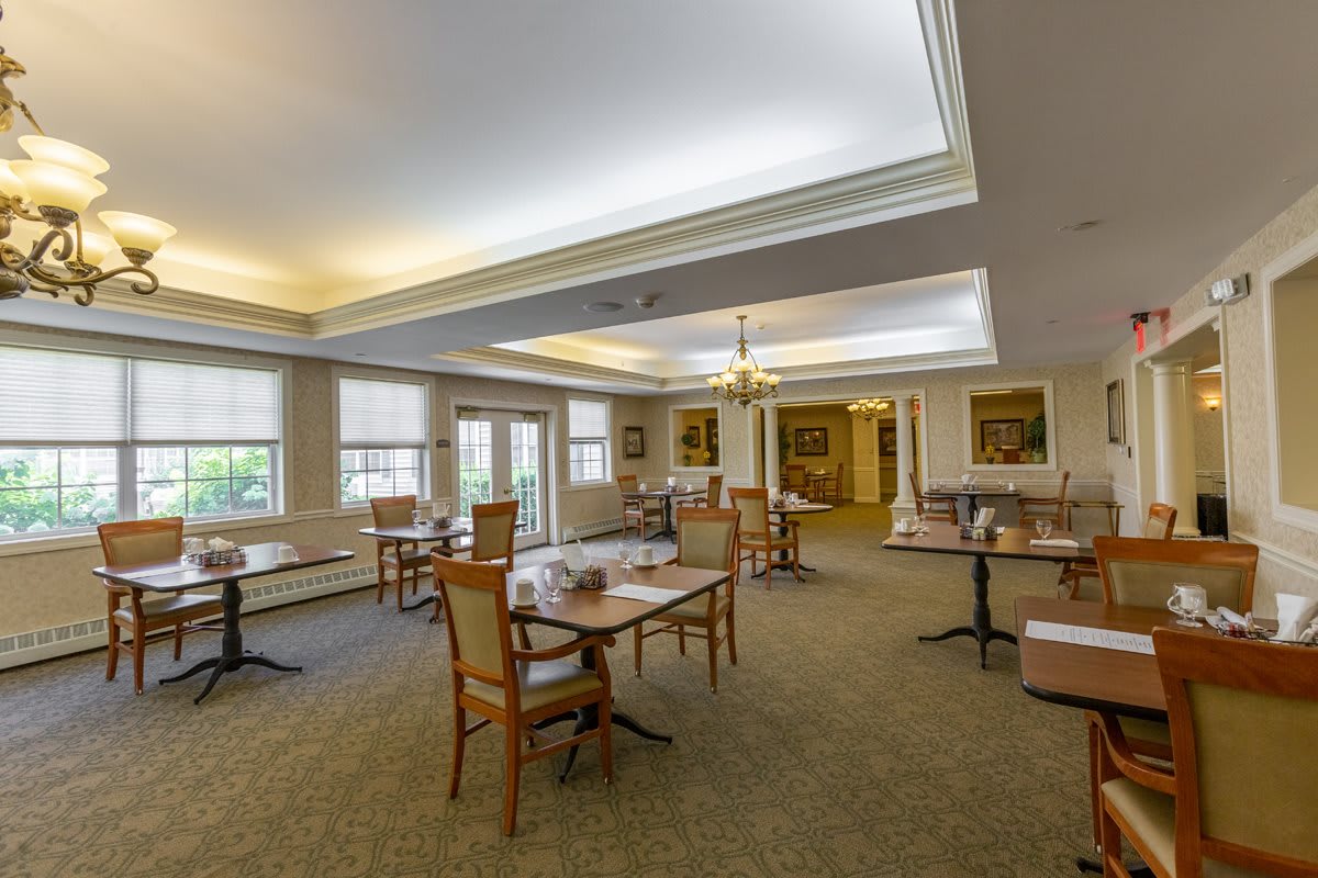 A spacious dining area with multiple tables and chairs, featuring large windows and elegant lighting.