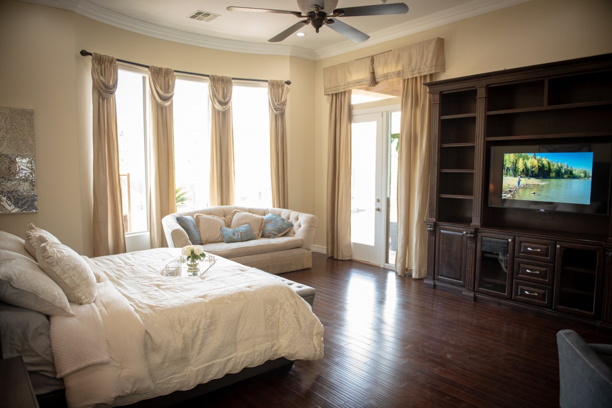 A cozy bedroom featuring a bed, sofa, and large windows with elegant curtains.