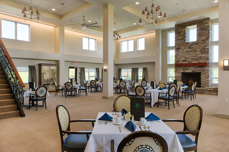 An elegant restaurant dining room with neatly arranged tables and chairs, featuring large windows and a chandelier.