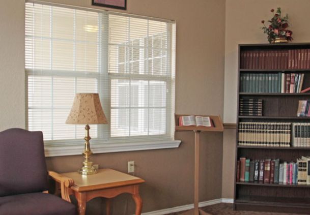A cozy reading nook with a window, lamp, and bookshelf filled with books.