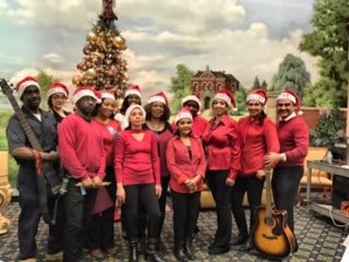 Group of people in festive clothing standing in front of a Christmas tree.