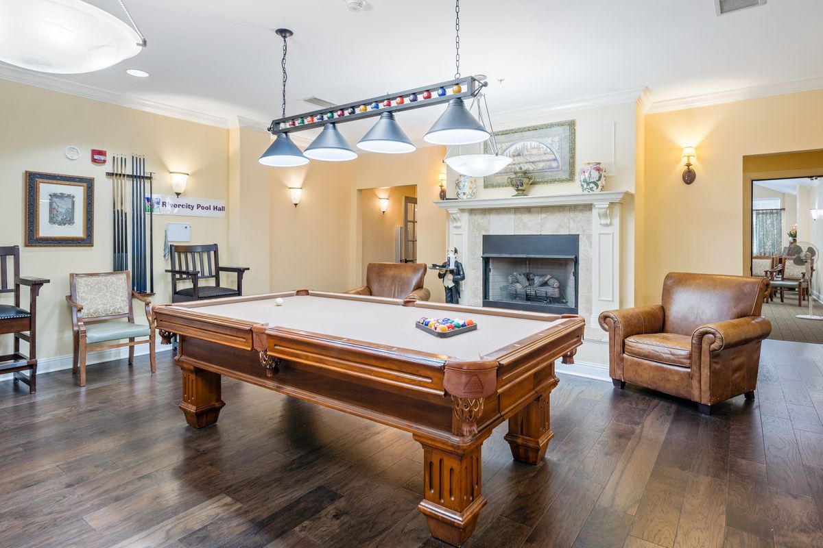 A cozy billiard room with a classic pool table, elegant lighting, and a warm fireplace.