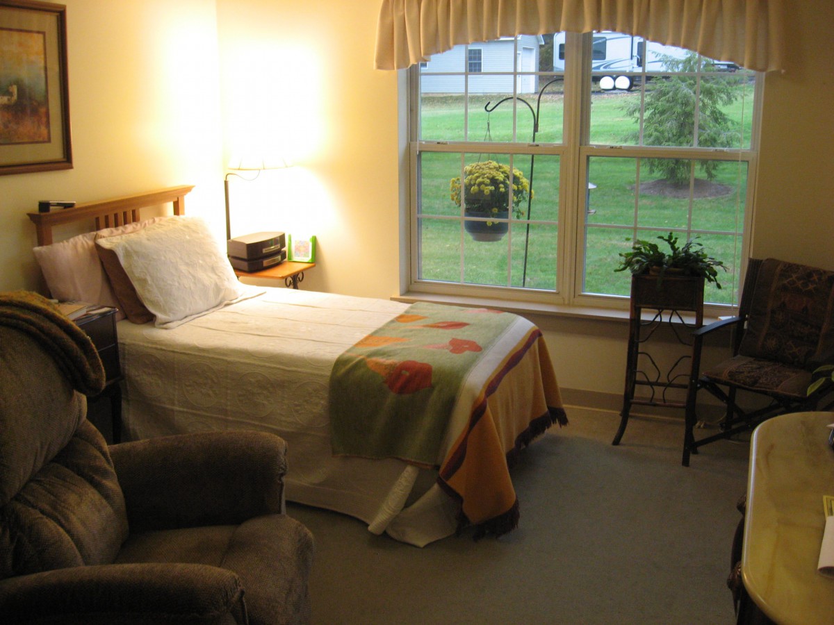 A cozy bedroom with a single bed, armchair, and a large window overlooking the garden.