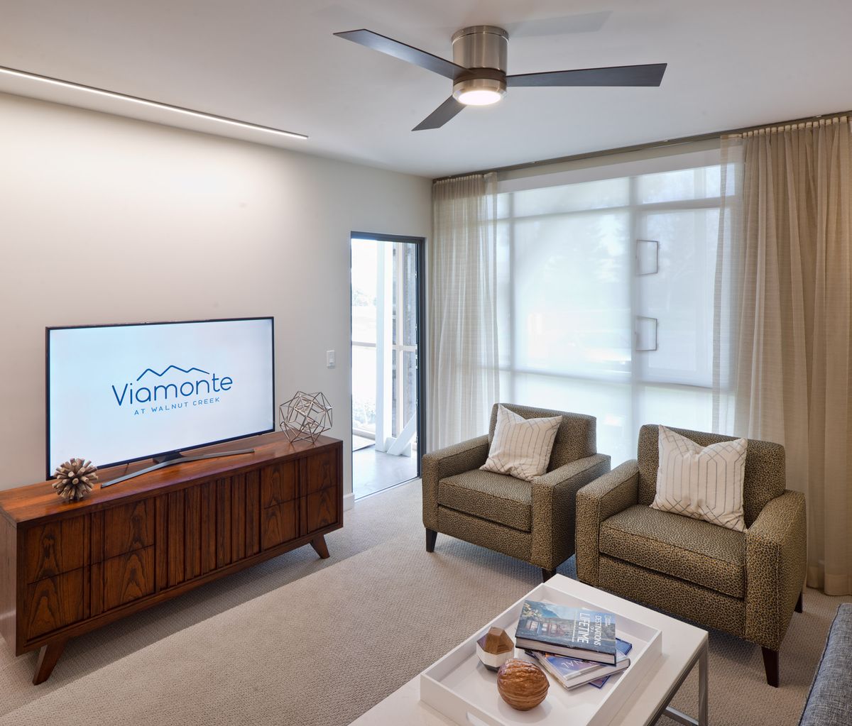 A modern living room with comfortable armchairs, a television, and a ceiling fan.