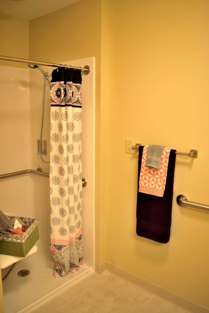 A bathroom with a patterned shower curtain, towels on a rack, and yellow walls.
