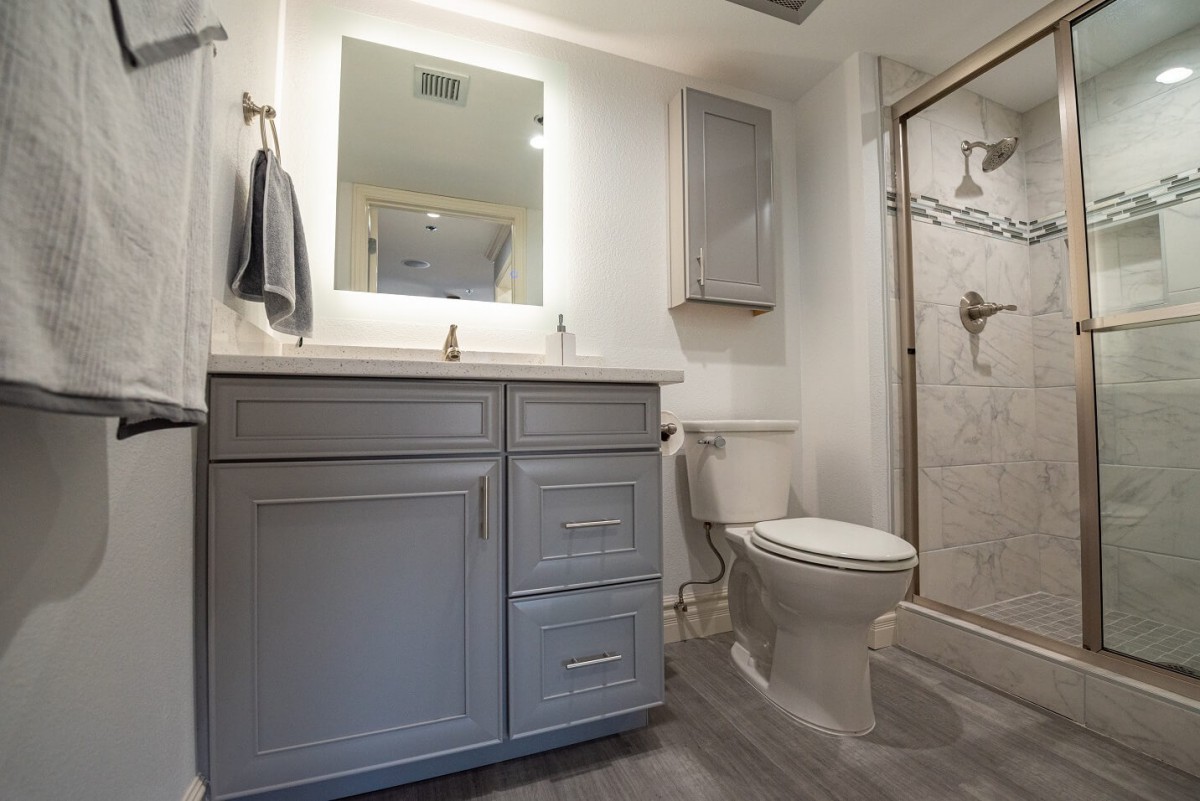 A modern bathroom with a vanity, mirror, toilet, and shower.