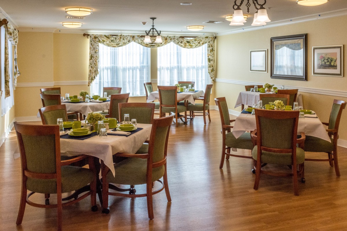 A well-appointed dining room with neatly arranged tables and chairs, featuring elegant decor and large windows with curtains.