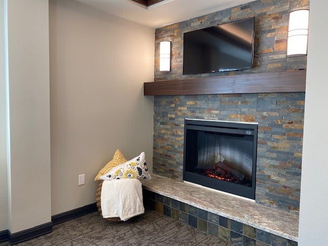 A modern living room featuring a cozy fireplace with a mounted TV above, accented by a stone wall, pillow, and blanket.