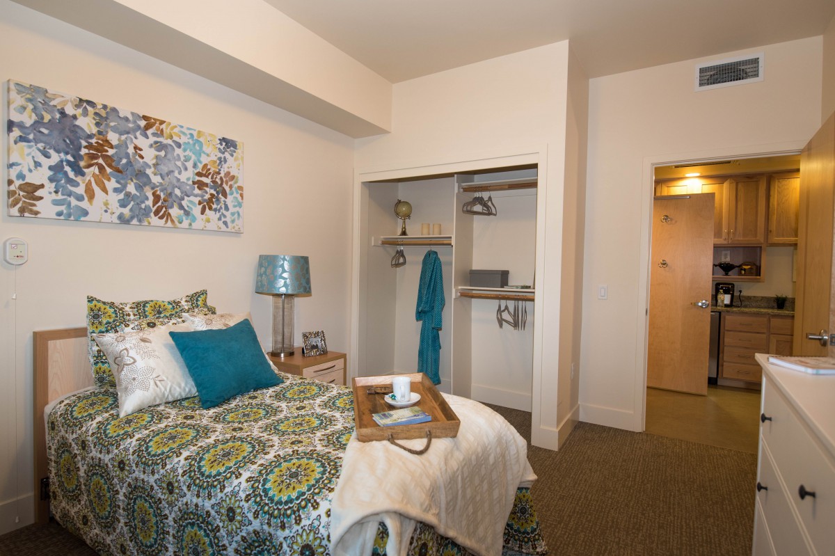 A cozy bedroom with a colorful bedspread, open closet, and decorative accents.