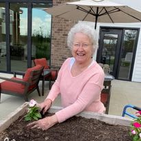 An elderly woman is happily gardening on a patio.