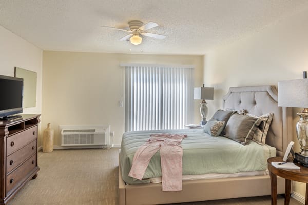 A cozy bedroom with a neatly made bed, ceiling fan, and soft lighting.