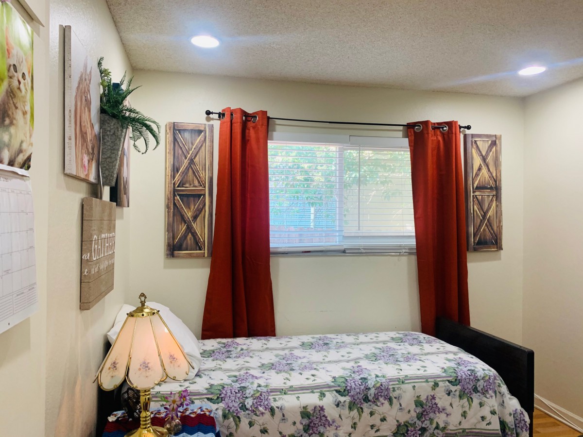 A cozy bedroom with red curtains and floral bedspread.