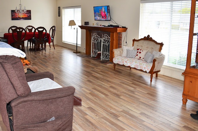 A spacious living room with hardwood floors, featuring a sofa, armchair, dining table, and a television mounted above a fireplace.