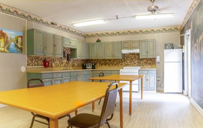 A spacious kitchen with wooden tables and chairs, equipped with cabinets and appliances.
