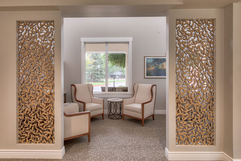 A cozy living room area with two armchairs and a small table, framed by decorative panels and a window view.