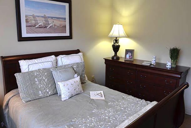 A cozy bedroom with decorative pillows, a lamp, and framed artwork on the wall.